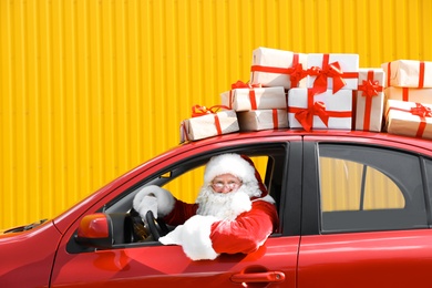 Authentic Santa Claus driving red car with gift boxes, view from outside