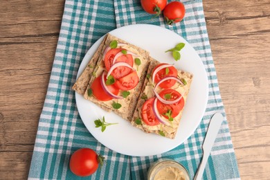 Photo of Fresh crunchy crispbreads with pate, tomatoes, red onion and greens on wooden table, flat lay