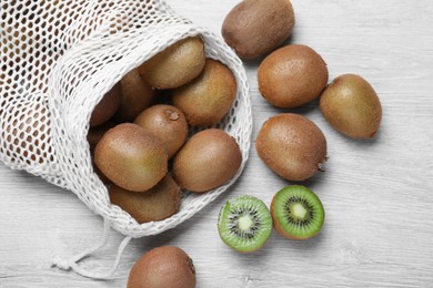 Photo of Net bag with cut and whole fresh kiwis on white wooden table, flat lay