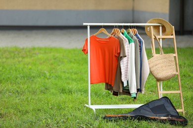 Photo of Clothing rack with different garments in yard, space for text. Garage sale