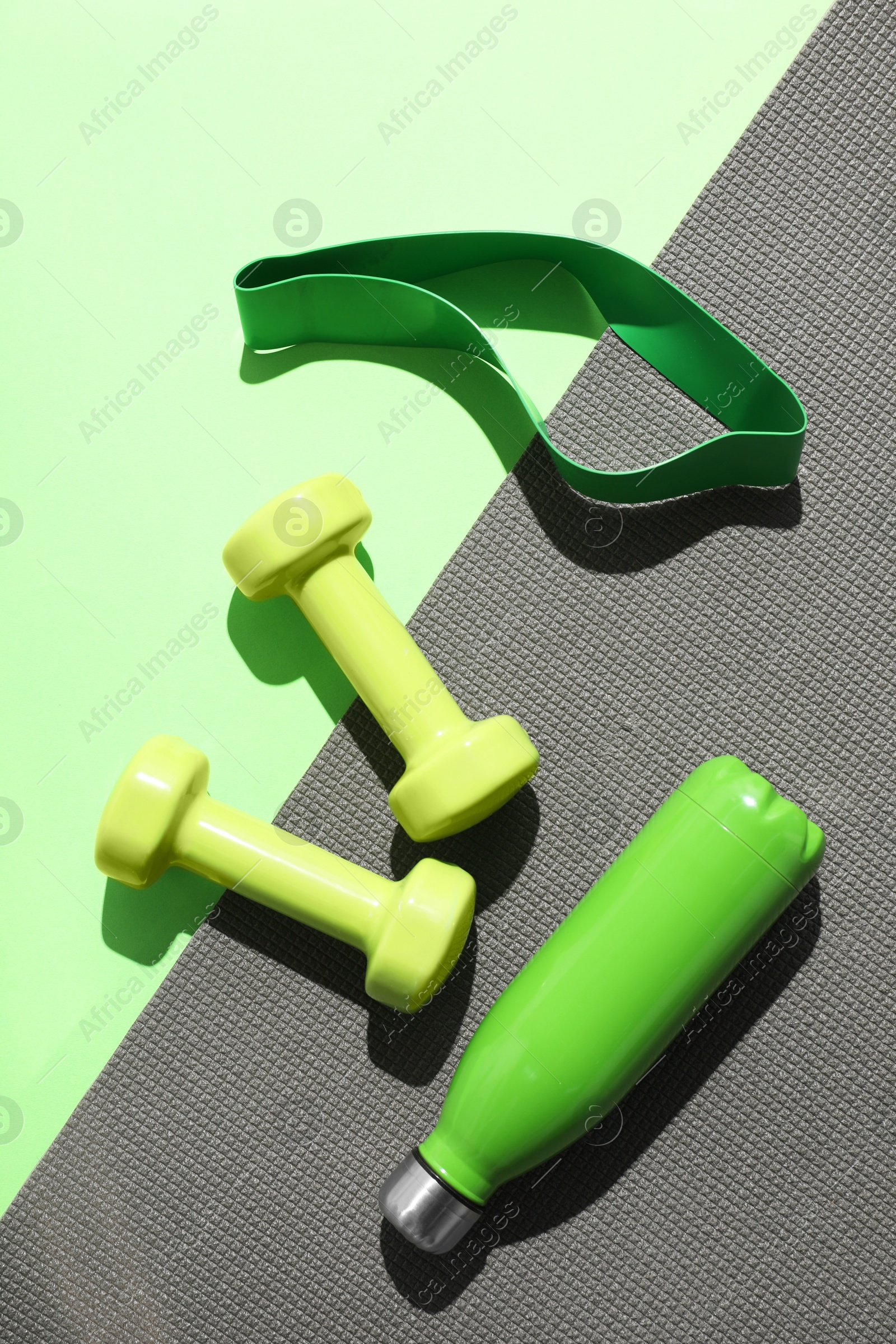 Photo of Dumbbells, fitness elastic band, water bottle and mat on light green background, flat lay