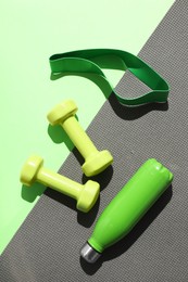 Photo of Dumbbells, fitness elastic band, water bottle and mat on light green background, flat lay