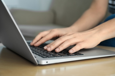 Photo of Woman working on modern laptop at wooden table indoors, closeup