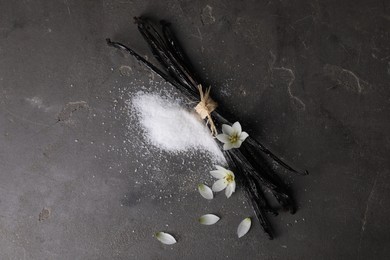 Photo of Vanilla pods, sugar, flowers and petals on gray textured table, flat lay. Space for text