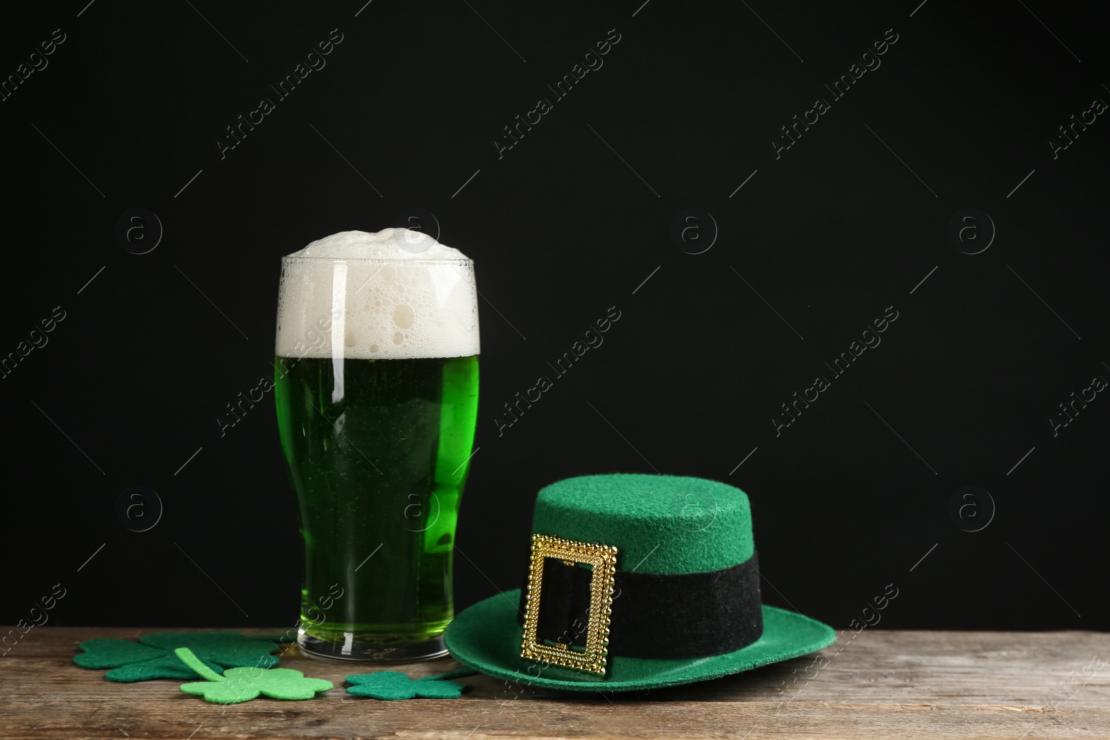 Photo of Green beer, hat and clover leaves on wooden table against black background. St. Patrick's Day celebration