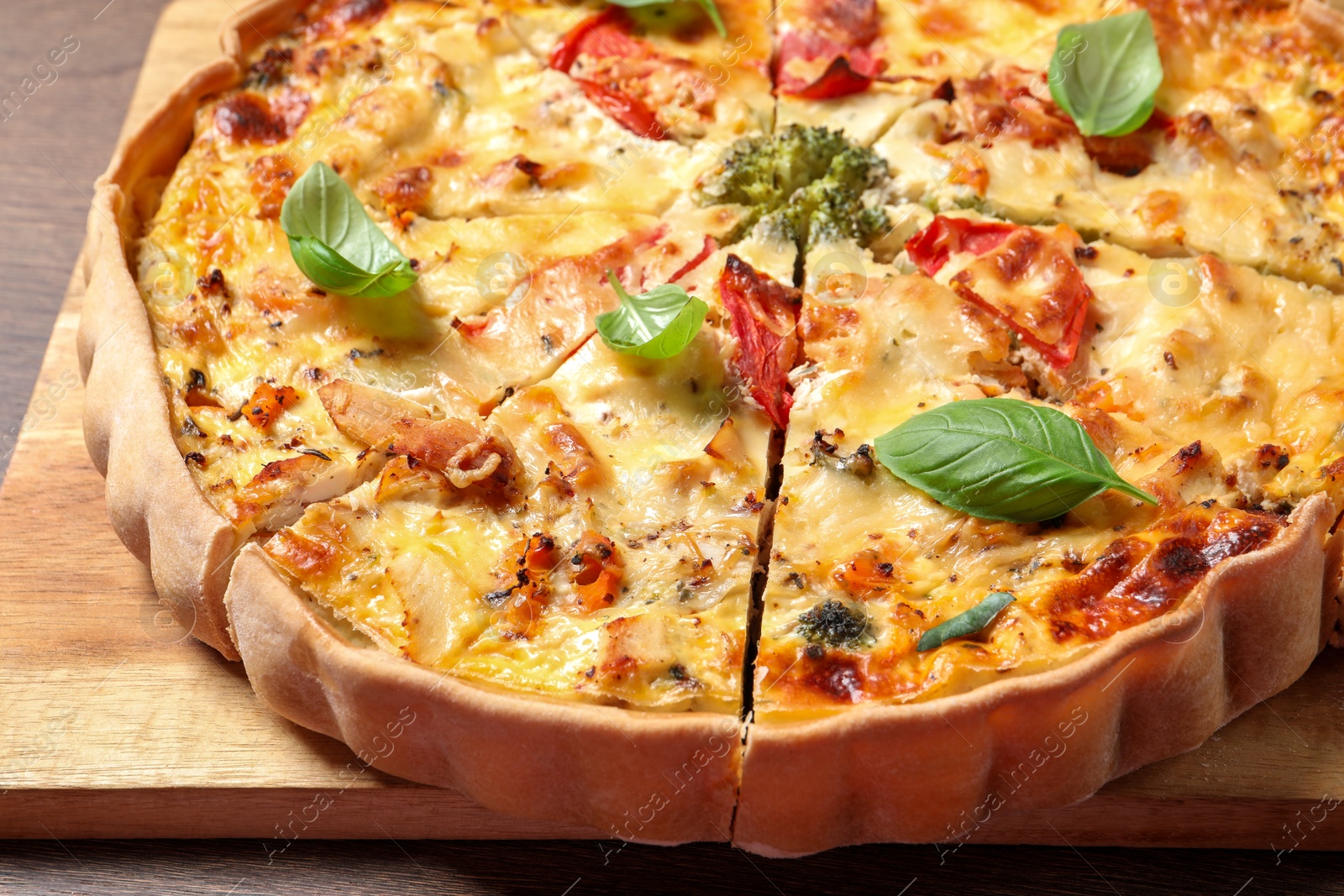 Photo of Tasty quiche with tomatoes, basil and cheese on wooden table, closeup