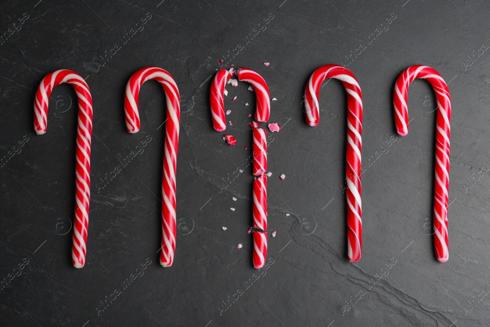 Photo of Crushed and whole Christmas candy canes on black background, flat lay