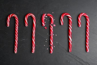Photo of Crushed and whole Christmas candy canes on black background, flat lay