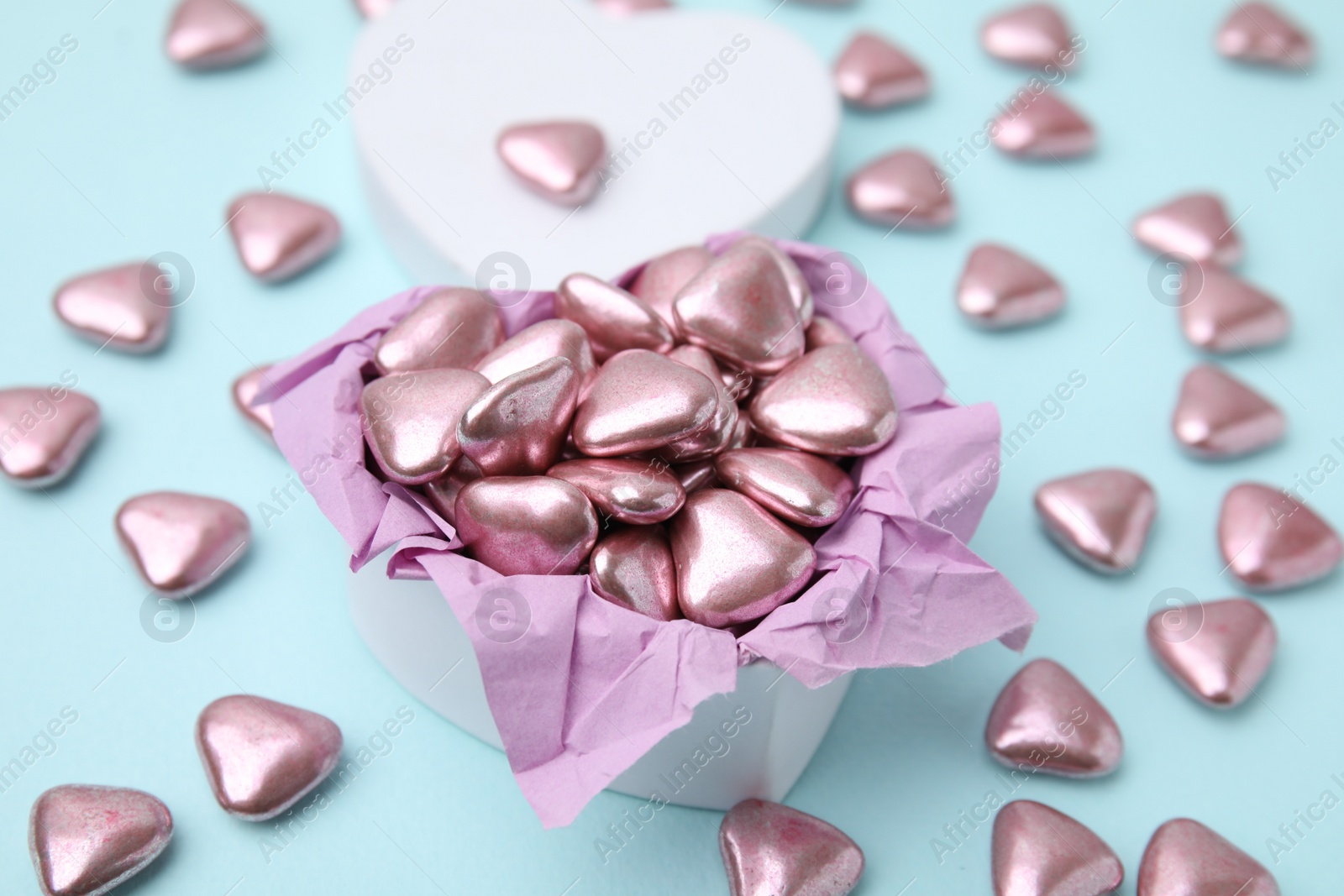 Photo of Box and delicious heart shaped candies on light blue background, closeup