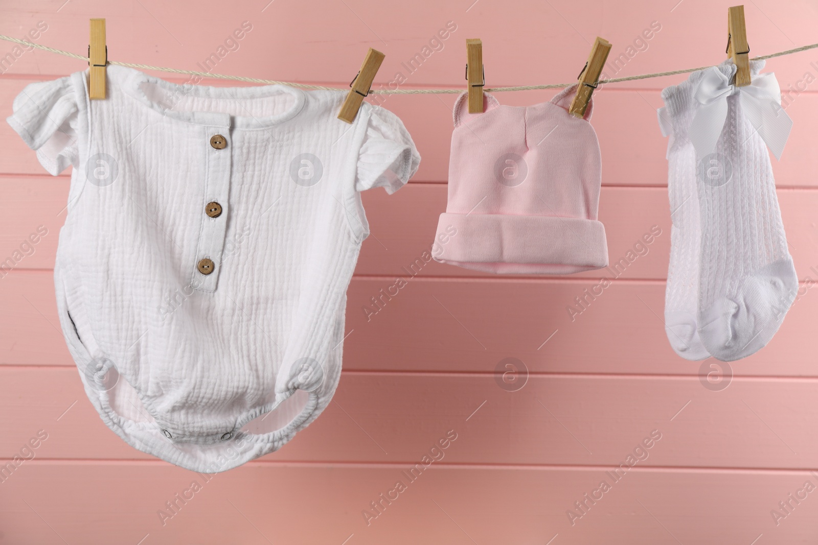 Photo of Baby clothes and accessories hanging on washing line near pink wooden wall