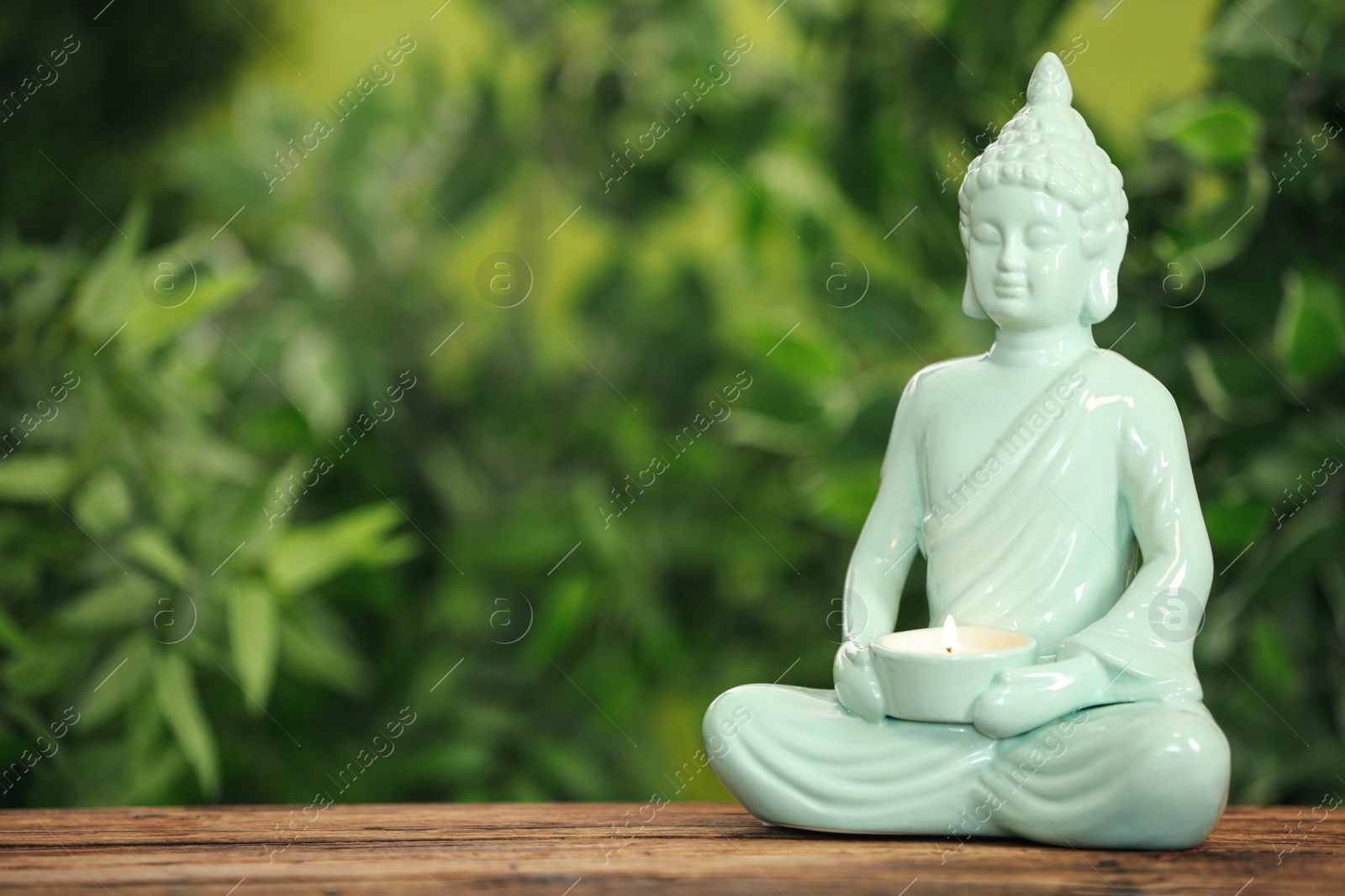 Photo of Buddha statue with burning candle on wooden table. Space for text