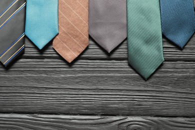 Different neckties on black wooden table, flat lay. Space for text