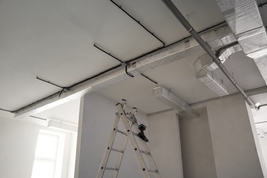 Conduits with cables and ventilation system on white ceiling, low angle view. Installation of electrical wiring