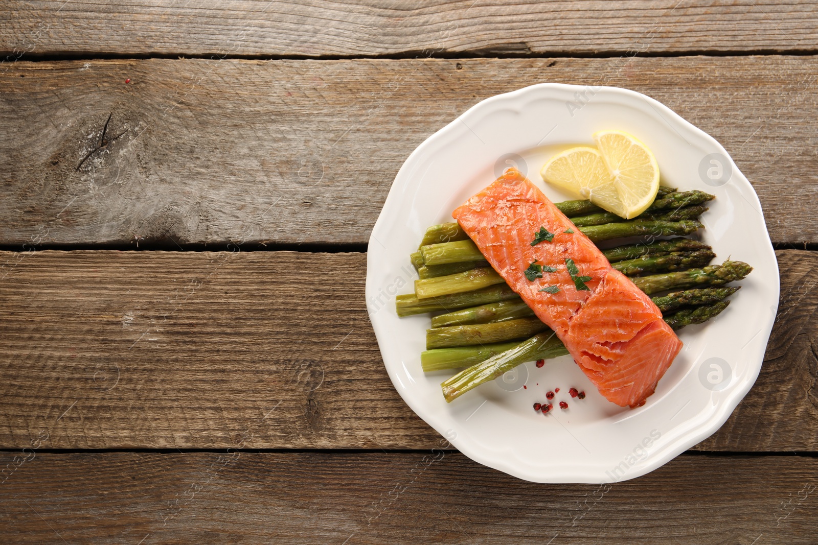 Photo of Tasty grilled salmon with asparagus and lemon on wooden table, top view. Space for text