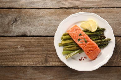 Photo of Tasty grilled salmon with asparagus and lemon on wooden table, top view. Space for text