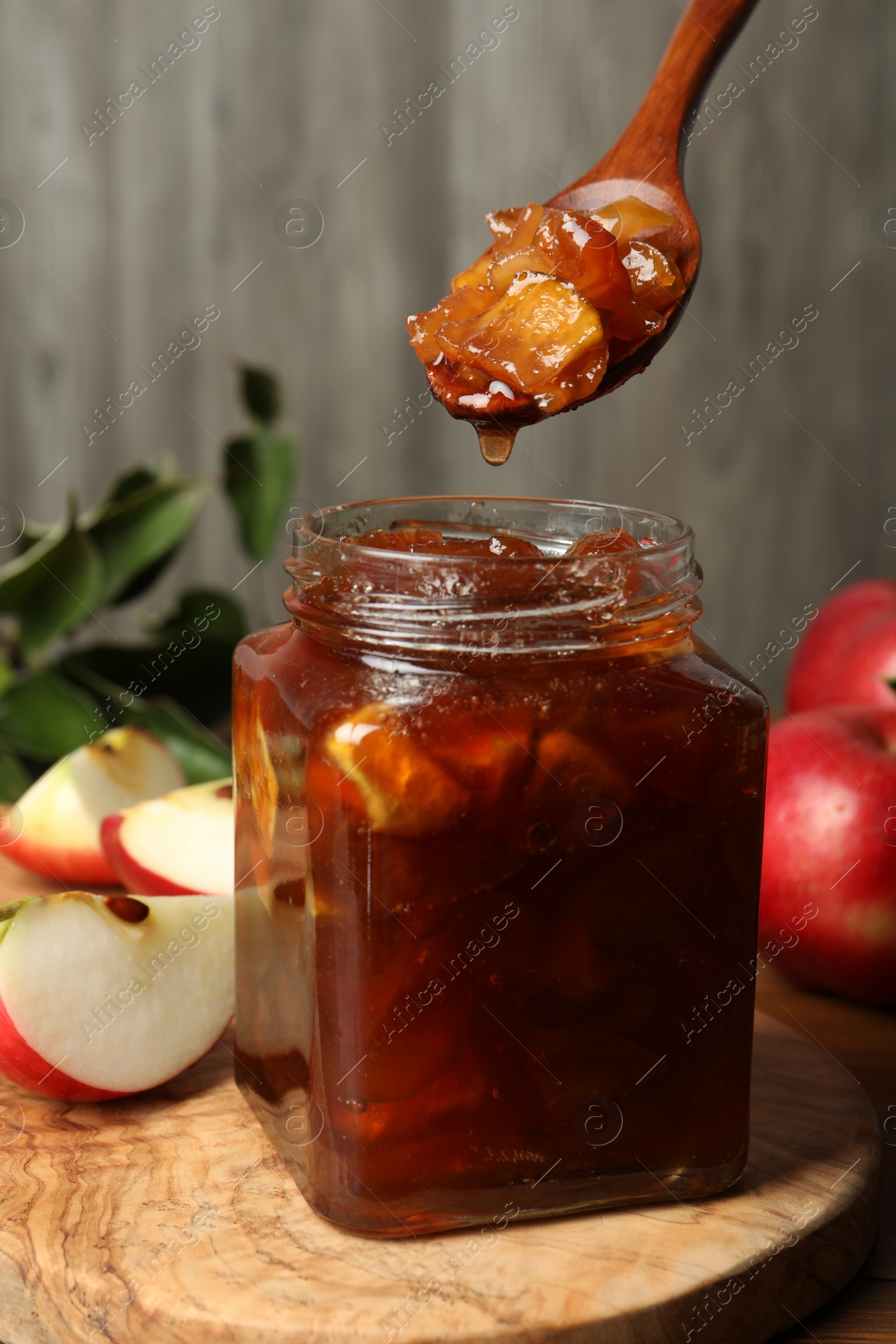 Photo of Spoon with tasty apple jam over glass jar at table