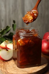 Photo of Spoon with tasty apple jam over glass jar at table