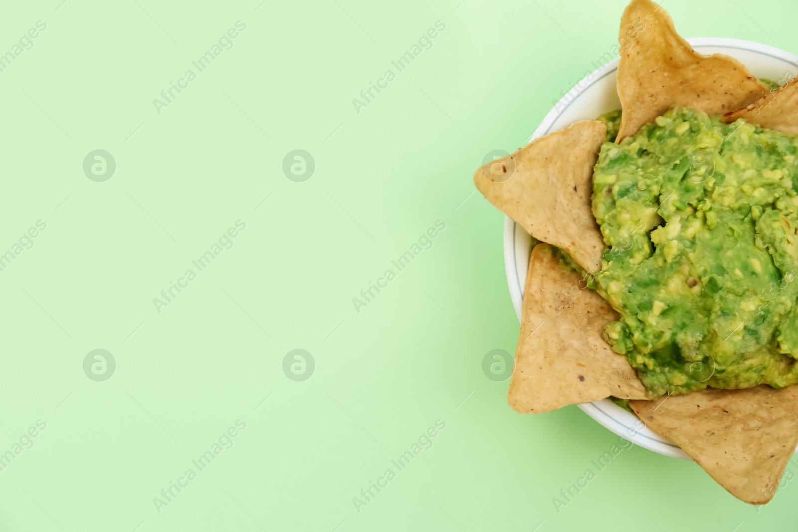Photo of Delicious guacamole made of avocados with nachos on light green background, top view. Space for text