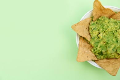 Delicious guacamole made of avocados with nachos on light green background, top view. Space for text