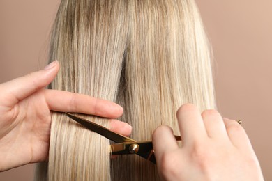 Hairdresser cutting client's hair with scissors on beige background, closeup