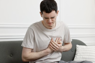 Photo of Young man suffering from heart hurt on sofa at home