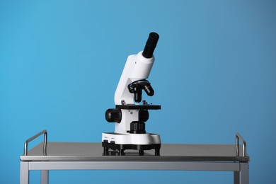 Photo of Modern microscope on metal table against blue background