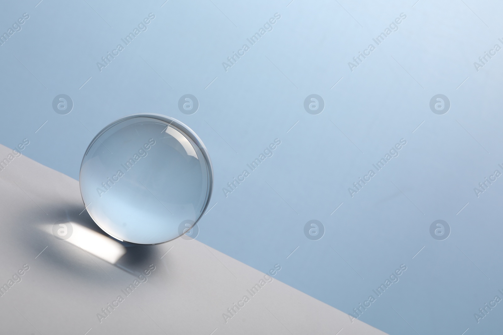 Photo of Transparent glass ball on table against light blue background. Space for text