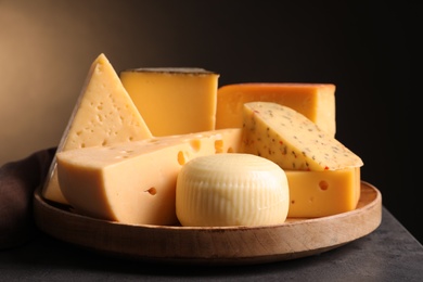 Photo of Wooden plate with different sorts of cheese on grey table