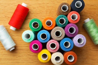 Photo of Many colorful sewing threads on wooden table, flat lay