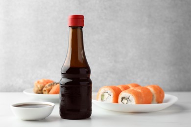 Photo of Tasty soy sauce and different types of sushi on white table