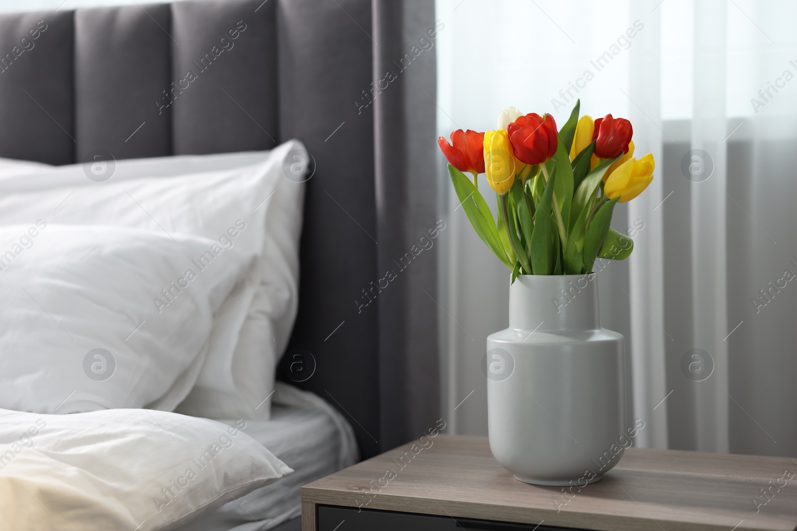 Photo of Beautiful tulips in vase on bedside table indoors