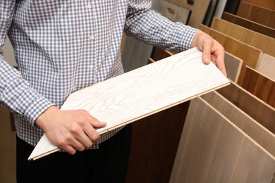 Man with sample of light wooden flooring in shop, closeup