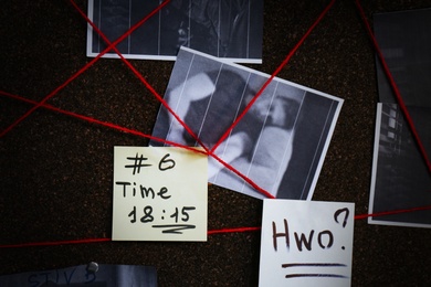 Photo of Detective board with crime scene photos, stickers, clues and red thread, closeup