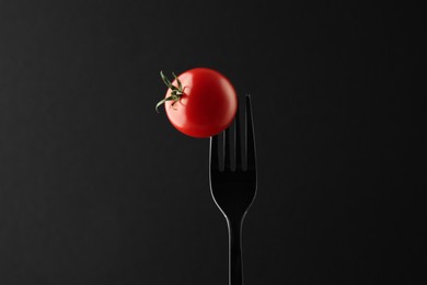 Photo of Fork with cherry tomato on black background