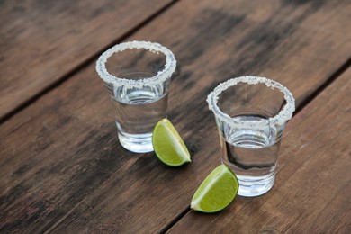 Mexican tequila shots with lime slices and salt on wooden table