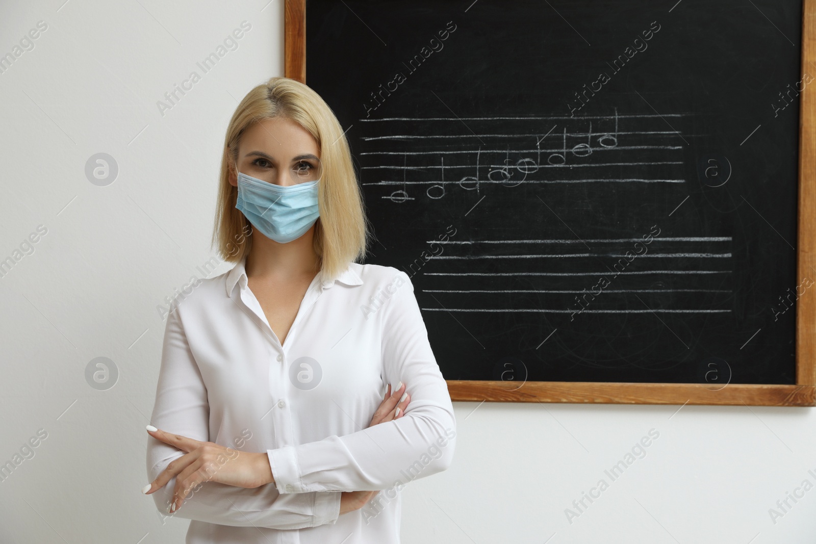 Photo of Teacher wearing protective mask near black chalkboard with music notes in classroom