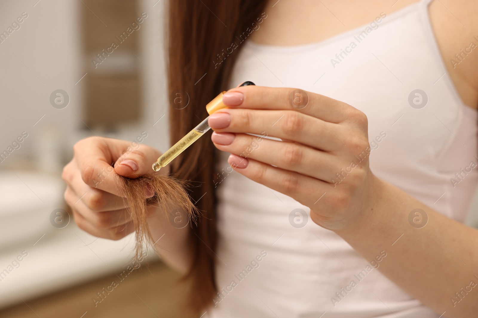 Photo of Woman applying oil hair mask indoors, closeup