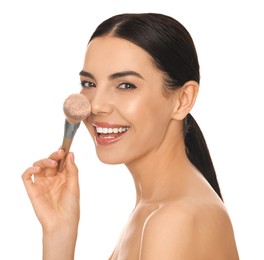 Beautiful young woman applying face powder with brush on white background