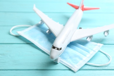 Photo of Toy airplane and medical mask on light blue wooden background, closeup. Travelling during coronavirus pandemic