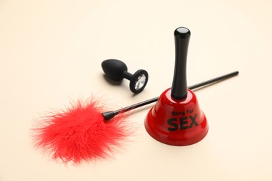 Photo of Bell with text Ring For Sex, feather teaser and anal plug on beige background
