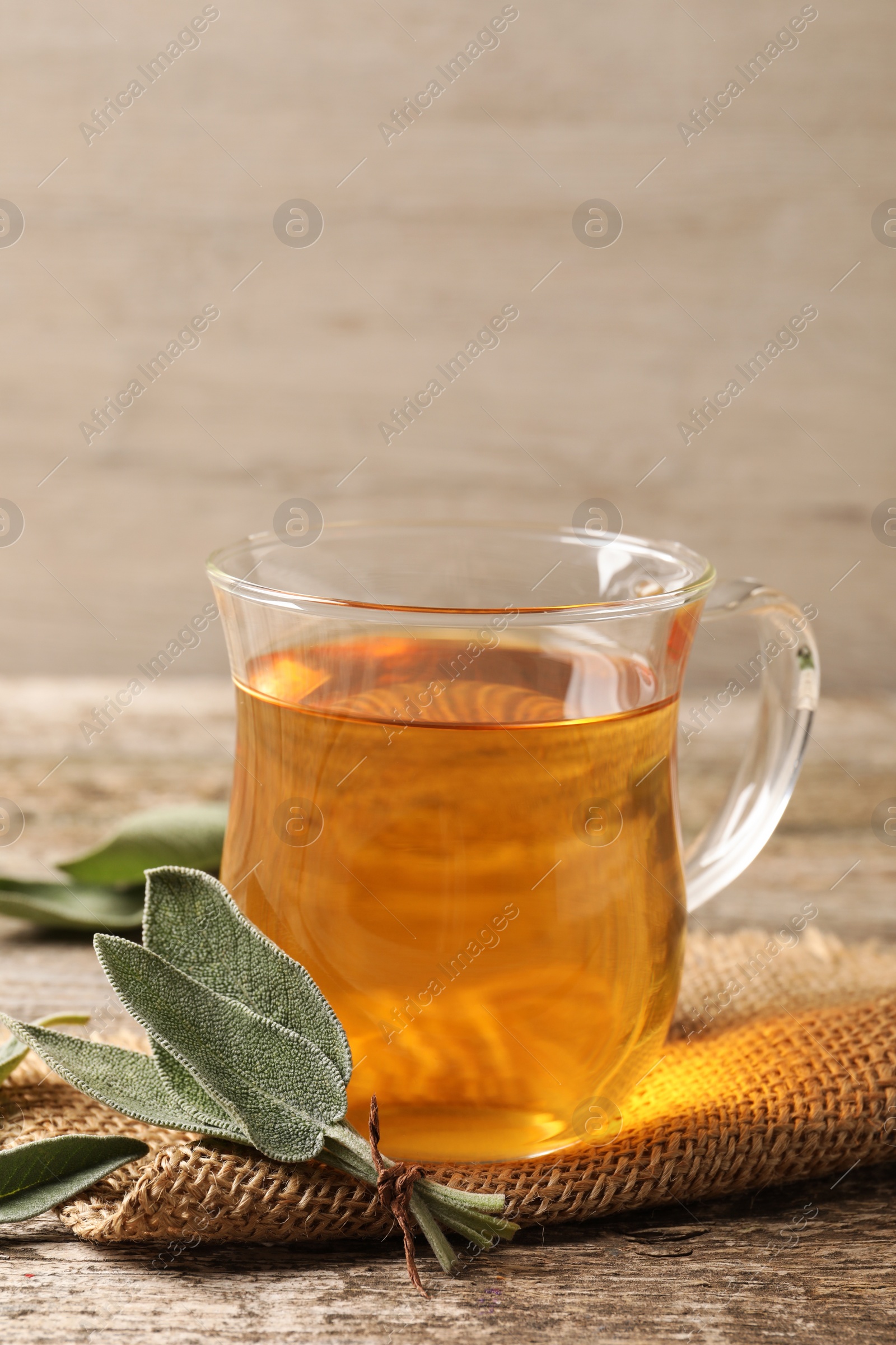 Photo of Cup of aromatic sage tea and fresh leaves on wooden table. Space for text