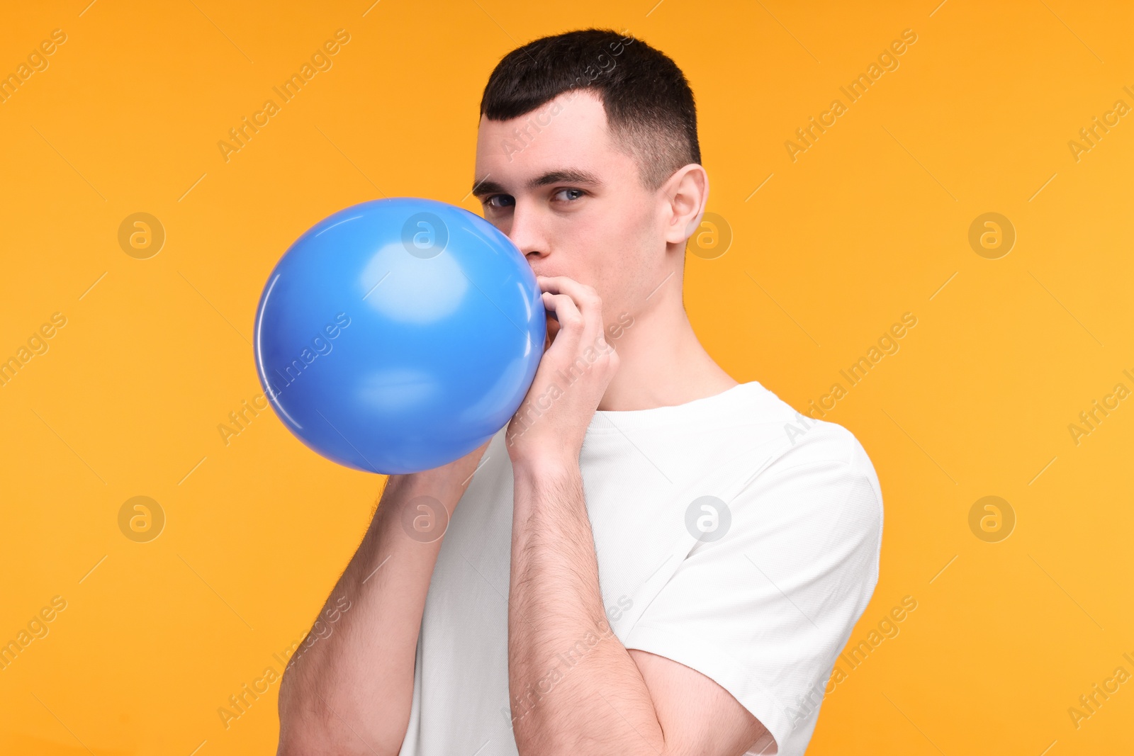 Photo of Young man inflating light blue balloon on yellow background