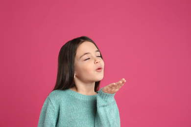 Cute little girl blowing air kiss on pink background