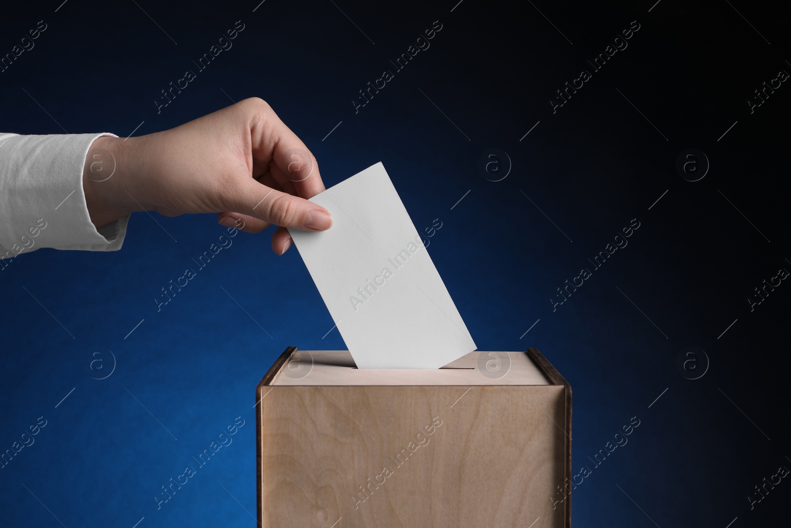 Photo of Woman putting her vote into ballot box on dark blue background, closeup