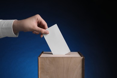 Photo of Woman putting her vote into ballot box on dark blue background, closeup