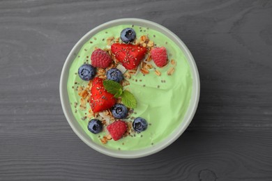 Photo of Tasty matcha smoothie bowl served with berries and oatmeal on grey wooden table, top view. Healthy breakfast