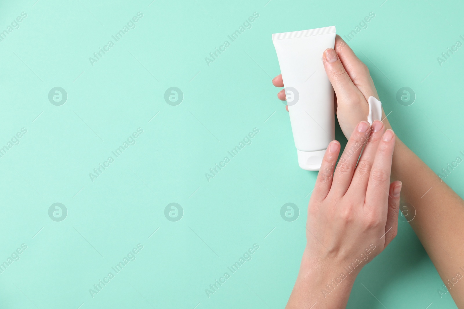 Photo of Woman with tube applying cosmetic cream onto her hand on turquoise background, top view. Space for text