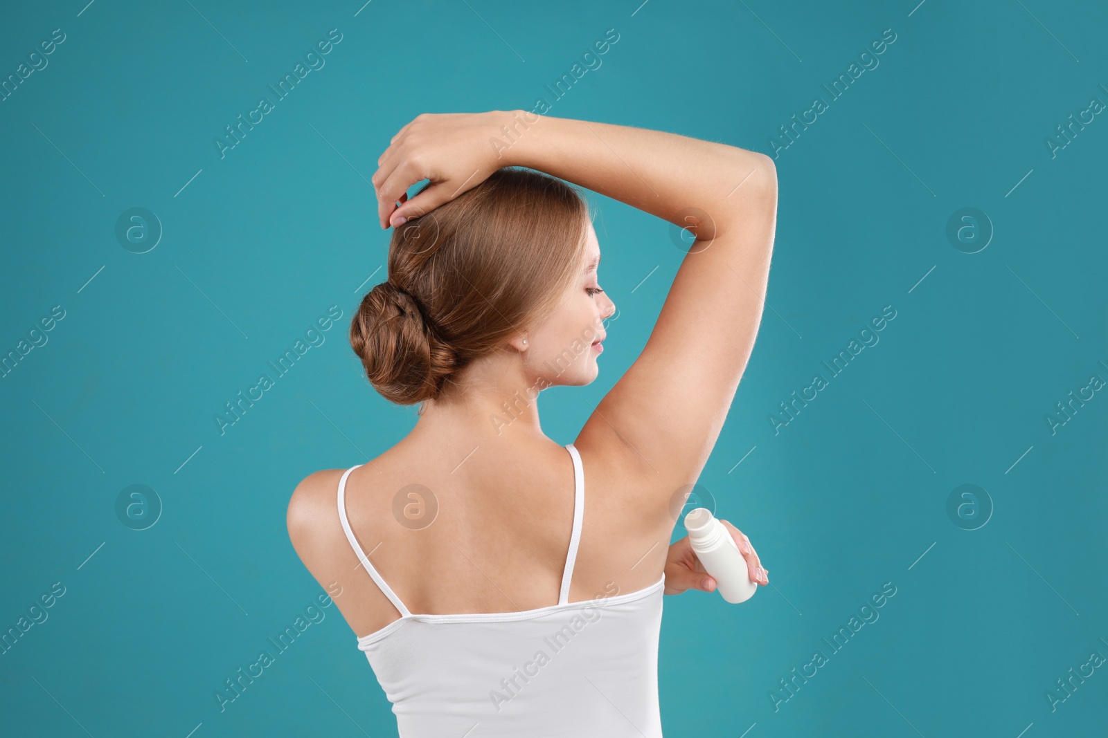 Photo of Young woman applying deodorant to armpit on teal background