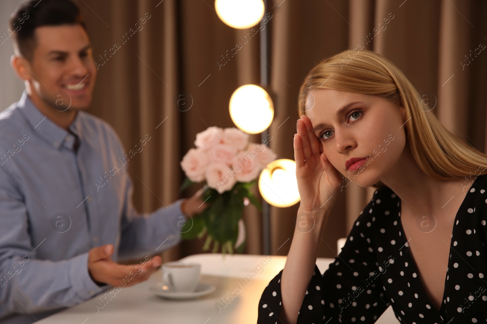 Photo of Man giving flowers to displeased young woman in restaurant. Failed first date