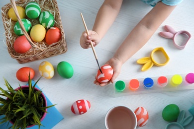 Photo of Little child painting Easter eggs on wooden background, top view